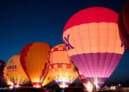 a group of hot air balloons with various corporate logos on them at night
