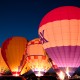 a group of hot air balloons with various corporate logos on them at night
