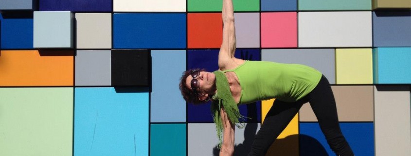 a woman in front of a colorful geometric wall doing a yoga pose