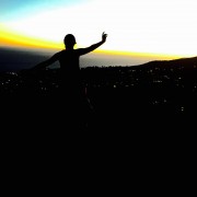 the silhouette of a person standing in front of a black skyline and colorful sky above