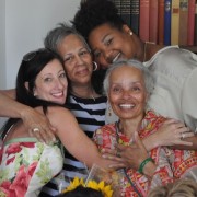 four women hugging each other with a bookshelf of books behind them