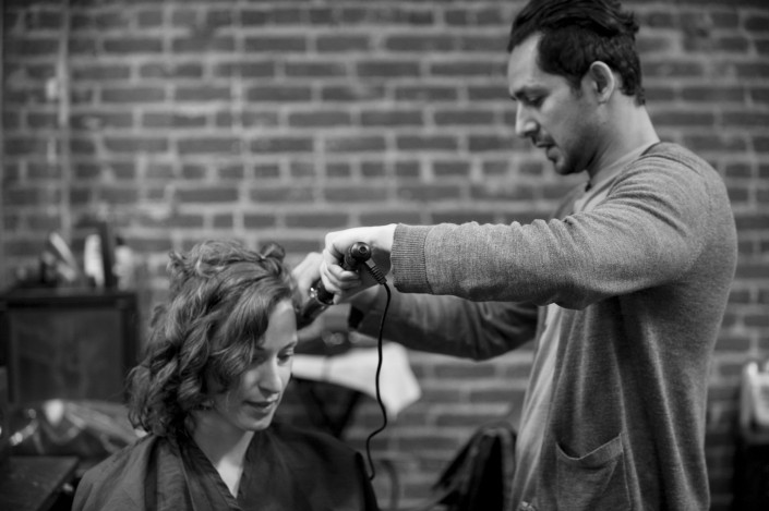 a black and white image of a woman getting her hair curled by a man in a sweater