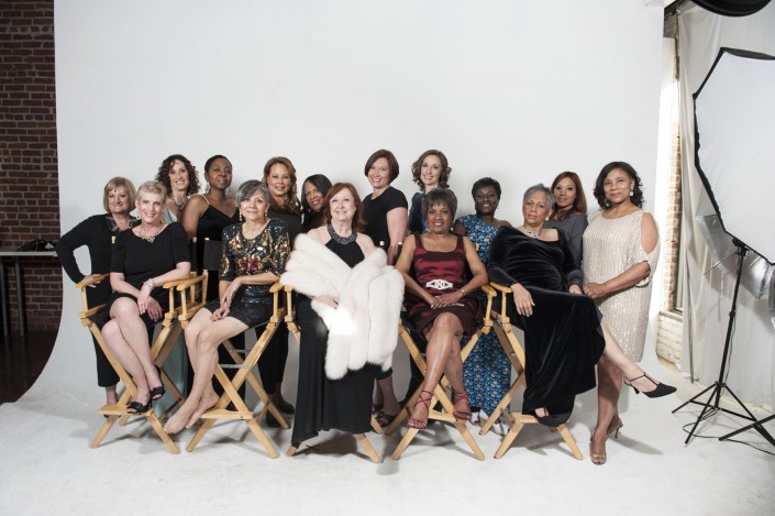 a group of women seated in director's chairs against a white backdrop