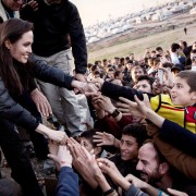 a woman in a black coat leaning down to touch the hands of people below her