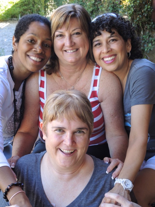 three women standing over a woman who is seated all smiling for the camera