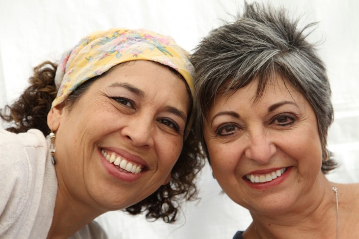 a woman wearing a yellow and pink scarf on her head leaning her forehead against a woman with spiked hair