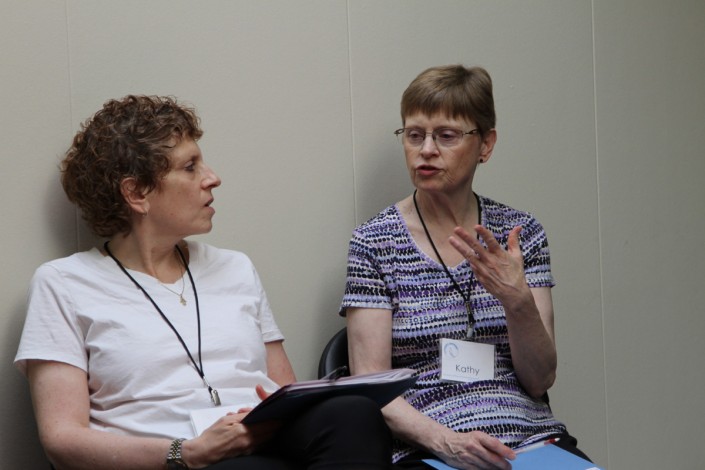 a woman in white seated beside a woman in a striped shirt and both are wearing lanyards