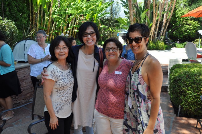 four women standing in a backyard with palm trees behind them and their arms around each othe