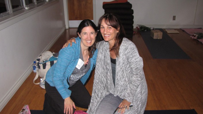 a woman in a blue sweater kneeling on the floor with a woman in a gray sweater