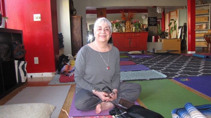 a woman dressed all in gray sitting crosslegged in a yoga studio