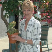 a woman in a white checked shirt holding a potted plant and stnading by a tree