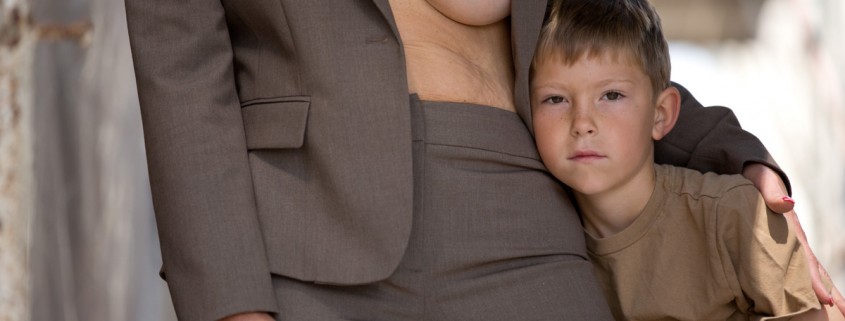 a young boy standing with a woman in a suit who is exposing one breast showing scars from surgery