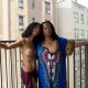 two women with breasts exposed showing surgery scars standing on a balcony in front of tall buildings