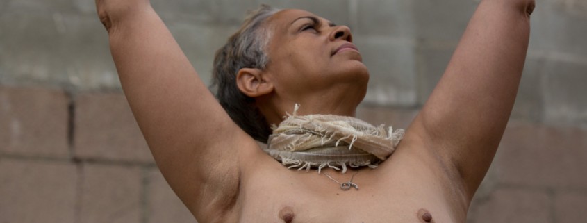 a woman wearing a scarf around her neck and no top showing her surgery scars with her arms lifted to the sky