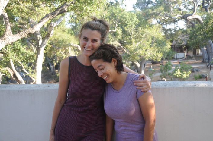 a woman leaning on another woman's chest while both are smiling and standing on a patio overlooking a garden