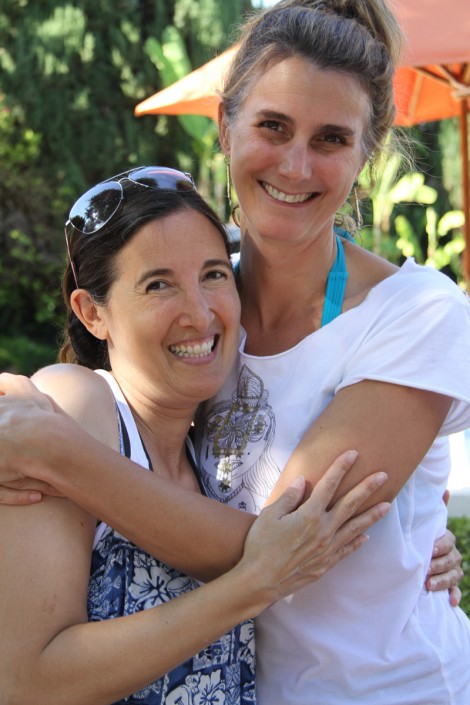 a tall woman in a white shirt with her arms around a shorter woman wearing a blue shirt and sunglasses on her head