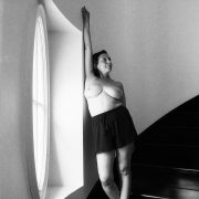 a black and white image of a woman exposing her breasts while wearing a black shirt and standing on a stairwell