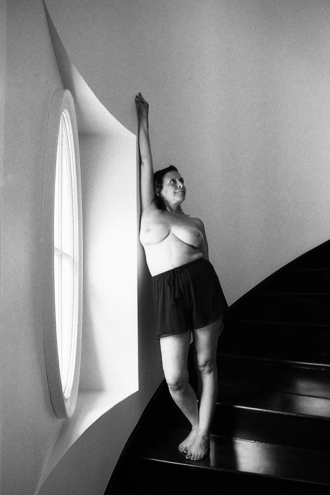 a black and white image of a woman exposing her breasts while wearing a black shirt and standing on a stairwell