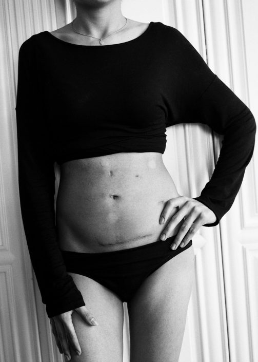 a black and white image of a woman's body from the neck down wearing black panties and black long sleeved shirt