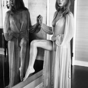a black and white image of a woman wearing only a robe standing in front of a mirror with one leg lifted
