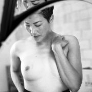 a black and white image of a woman with short hair exposing one breast while covering the other with her arm