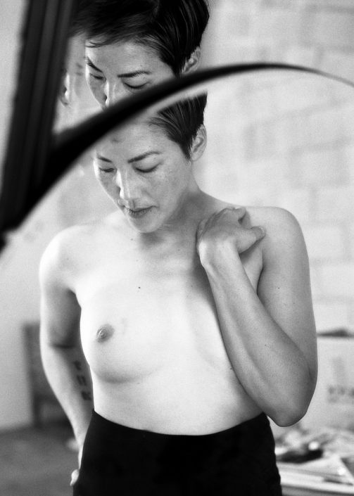 a black and white image of a woman with short hair exposing one breast while covering the other with her arm