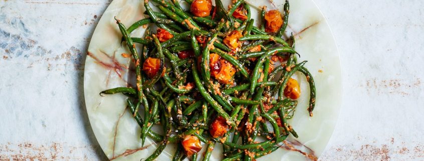 a plate of green beans with tomatoes on a marble dish