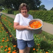 a woman in a white shirt holding a bucket of orange flowers while standing in a field