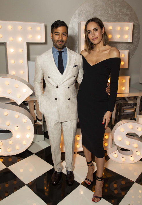 a man in a white suit standing beside a woman in a black dress with lit letters behind them