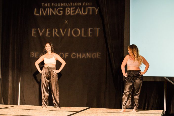 two women in white bras and black drawstring pants posing in front of a black curtain