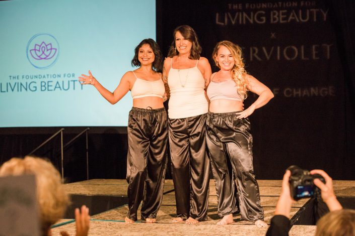 three women in white tops with black drawstring pants posing in front of an audience on a runway