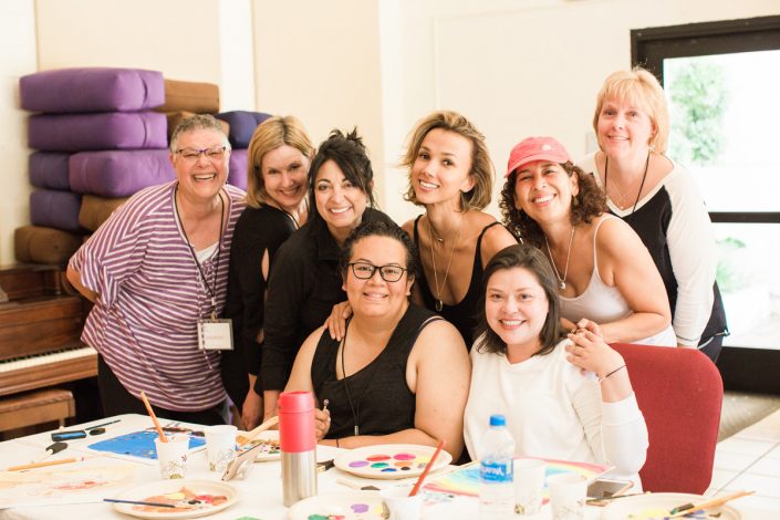 a group of women smiling for the camera with table of paint supplies