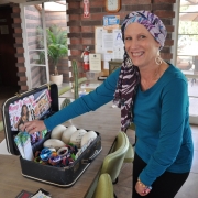 a woman in a blue sweater wearing a scarf on her head standing by a table set with a suitcase of products