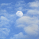 the moon in a blue sky with puffy clouds