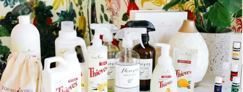 a collection of Thieves products in white bottles set on a table with a floral wallpaper background behind htem