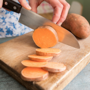 a knife shown cutting into a sweet potato on a cutting board
