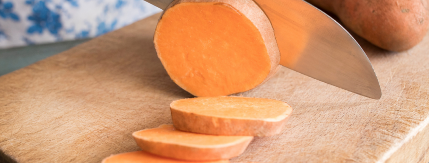 a knife shown cutting into a sweet potato on a cutting board