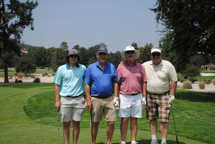 four men in golfing attire standing together on a golf course by a sand trap