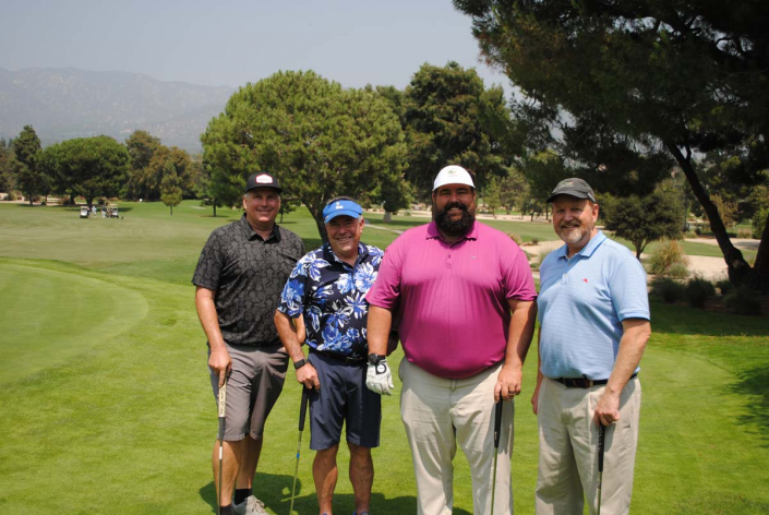 four men wearing golf attire posing on a golf course