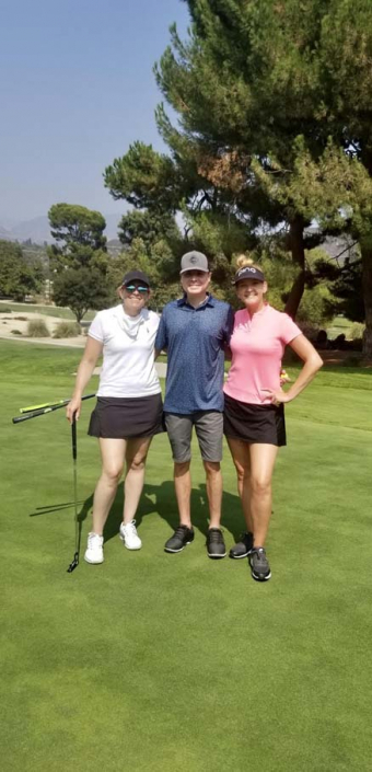two women and a man posing on a golf course with their arms around each other
