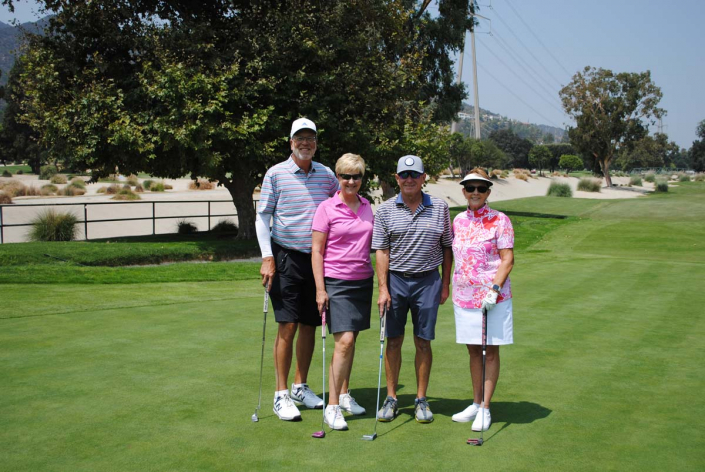 two women and two men posing on a golf course with their clubs