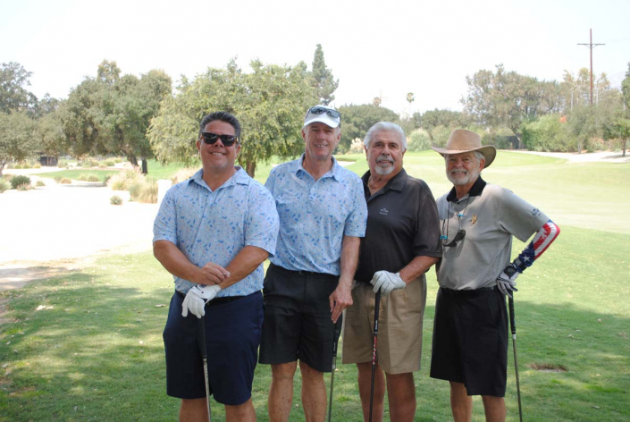 four men posing on the golf course with trees in the background