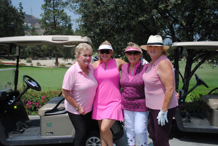 four women in golf gear standing in front of a golf cart